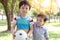 Handsome older brother holding ball and ready for playing in the park with younger brother. Little boy is always accompanied with