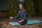 Handsome peaceful confident male athlete, a yogi with rosary beads, meditating in lotus pose on a yoga mat at sunset