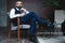 Handsome pensive man is touching his beard, looking away and thinking while sitting in armchair indoors.