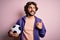 Handsome player man with beard playing soccer holding football ball over pink background pointing and showing with thumb up to the