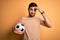 Handsome player man with beard playing soccer holding footballl ball over yellow background worried and stressed about a problem