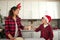 Handsome preadolescent boy in Santa hat bringing a bottle with milk to his loving mother cooking dough for Christmas cookies in