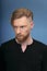 Handsome redhaired bearded man, wearing black shirt, posing frontal in studio, looking seriously, over blue background.