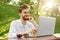 Handsome redhead european writer with stylish hairstyle and beard, sitting in sunny park, looking at camera, working on