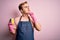 Handsome redhead man doing housework wearing apron and gloves using cleaner scourer serious face thinking about question with hand