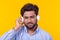 Handsome relaxed indian man with beard is listening to favorite music at the earphones on yellow background. Music