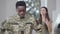 Handsome sad stressed African American man in military camouflage standing at home as blurred angry Caucasian woman