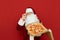 Handsome Santa Claus in glasses isolated on red background with pizza box in his hands, adjusts glasses and looks into the camera
