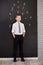 Handsome school boy in googles white shirt tie standing close to school desk with numbers above around the head.