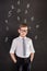 Handsome school boy in googles white shirt tie standing close to school desk with numbers above around the head.