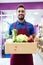 Handsome sellman holding a box with fruits and vegetables in fruitshop.