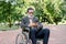 Handsome senior concentrated bearded man sitting in wheelchair in park, bowing his head while looking at screen of his