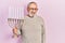 Handsome senior man with beard holding menorah hanukkah jewish candle looking positive and happy standing and smiling with a