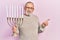 Handsome senior man with beard holding menorah hanukkah jewish candle smiling happy pointing with hand and finger to the side