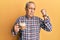 Handsome senior man with grey hair drinking a cup coffee strong person showing arm muscle, confident and proud of power