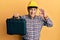 Handsome senior man with grey hair wearing safety helmet holding toolbox doing ok sign with fingers, smiling friendly gesturing