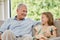 Handsome senior man and his granddaughter sitting on a sofa in the living room at home. Little girl visiting her grand