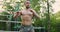 Handsome shirtless sportsman building muscles training with resistance band in nature