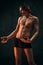 Handsome shirtless young guy with relief, muscular, fit body shape standing shirtless against dark textured studio