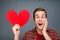 Handsome shocked young man holding red paper heart