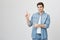 Handsome sincere young man in denim clothes pointing up and down and smiling at camera, over white background. Student