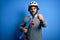 Handsome skater man with beard wearing security helmet holding skate over blue background annoyed and frustrated shouting with