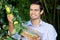 Handsome smiling farmer picking green apples from tree with basket.