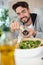 handsome smiling man salting salad in bowl at kitchen table