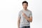 Handsome smiling man in t-shirt pointing aside and looking at promotional offer, shows banner and looks pleased, stands