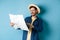 Handsome smiling tourist in straw hat looking at map, choosing travel road, planning a vacation, standing on blue