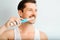 Handsome smiling young man brushing white teeth with modern electric toothbrush indoors. Happy man and trendy electric device