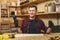 Handsome smiling young man working in carpentry workshop at wooden table place with piece of wood