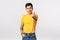 Handsome and stylish hipster asian guy in yellow t-shirt, with tattoos, extend arm and showing korean heart love sign