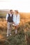 Handsome stylish man in rustic suit and pretty boho woman in dress, jacket, hat and cowboy boots, walking in the field