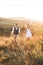 Handsome stylish man in rustic suit and pretty boho woman in dress walking in the field with straw bales, holding hands