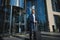 Handsome successful confident businessman in a business suit with black luggage against the background of a glass entrance to a