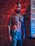 A handsome tattoed shirtless male with a stylish haircut and beard, standing against a brick wall in a room with a loft