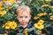 The handsome toddler stands among the tall yellow flowers and stares intently into the frame.