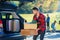 Handsome trendy bearded man loads luggage into the car trunk going on a family vacation trip.