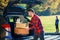 Handsome trendy bearded man loads luggage into the car trunk going on a family vacation trip.