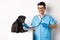 Handsome veterinarian at vet clinic examining cute black pug dog, pointing finger at pet during check-up with