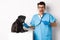 Handsome veterinarian at vet clinic examining cute black pug dog, pointing finger at pet during check-up with