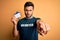 Handsome volunteer man with beard holding id card identification over yellow background pointing with finger to the camera and to