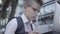 Handsome well-dressed boy in glasses sitting on the street working on the laptop close-up. Serious kid acting like adult