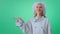 Handsome woman baker in a green studio wall looking straight to the camera smiling large and rise the hand up and keep