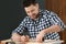 Handsome working man making marks on timber at table. Home repair