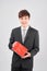 Handsome yound man in suit is posing on white background with red gift box in hands, looking at camera and smiling