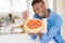 Handsome young african man holding and showing smiling proud homemade pepperoni pizza