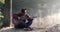 Handsome young asian man playing guitar at coast of forest river at sunrise. Dawn misty fog at background