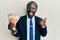 Handsome young black man wearing business suit holding 50 euros banknotes pointing thumb up to the side smiling happy with open